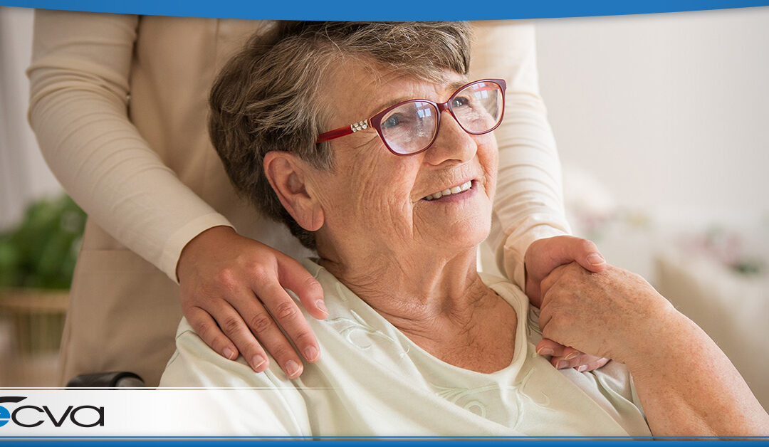 Elderly white woman sitting down. She is smiling and holding someone's hand